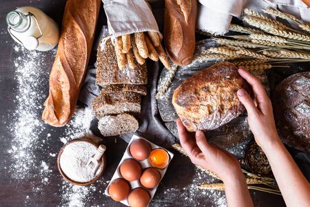 Concept of homemade bread, natural farm products, domestic production. Healthy and tasty organic food. Woman baked round whole grain bread. Top view flat lay, dark black background.の写真素材