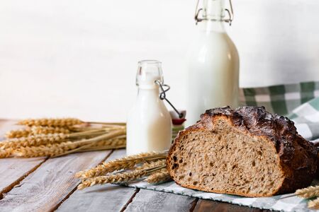 Concept of homemade bread, natural farm products, domestic production. Healthy and tasty organic food. Bread, milk, flour. Wheat spica as decor. Closeup, wooden backgroundの写真素材