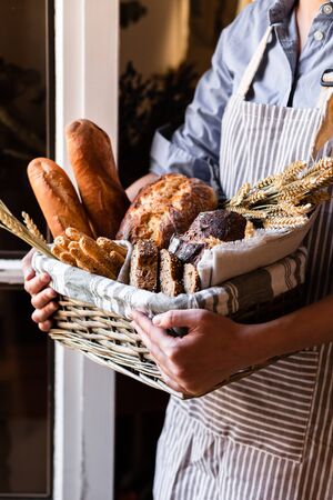 Concept of homemade bread, small bakery, natural farm products, domestic production. Healthy and tasty organic food. Woman holding basket with various bread freshly baked. Close upの写真素材