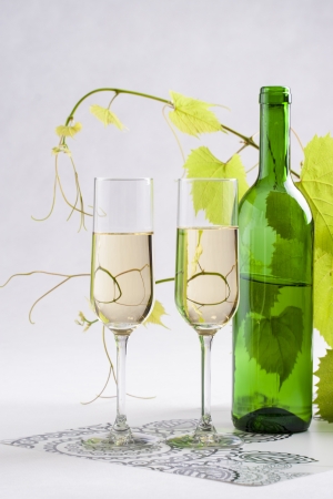 White wine glass and bottle with a grape leafs on a solid bright backgroundの写真素材