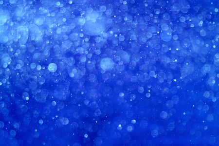 Blue Christmas background. It is made from photo of real snow fall. This blurred snowing in warm lights can be a Christmas, New Years eve or winter background texture.の写真素材