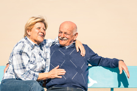 Happy senior couple in love having fun at the beach - Joyful elderly lifestyle with man and her wife laughing outdoors on a benchの写真素材