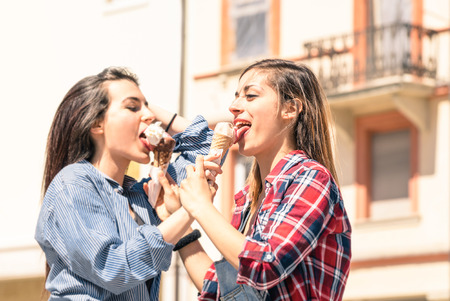 Young women best friends sharing an ice-cream during a sunny day walking around in the city center - Concept of carefree friendship during spring enjoying the upcoming summerの写真素材