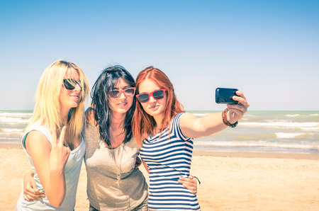 Group of girlfriends taking a selfie at the beach - Concept of friendship and fun in the summer with new trends and technology - Best friends enjoying the moment with modern smartphoneの写真素材