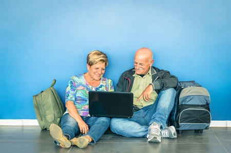 Happy senior couple sitting on the floor with laptop waiting for a flight at the airport - Concept of active elderly and interaction with new technologies - Travel lifestyle without age limitationの写真素材