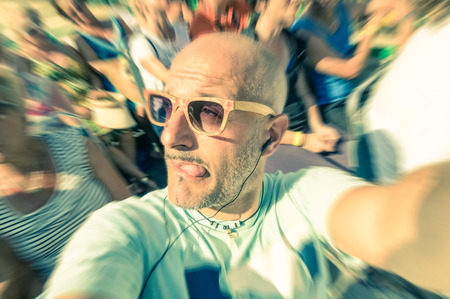 Bald funny man taking a selfie in the crowd with stupid tongue out expression - Travel lifestyle enjoying moment of carefree loneliness - Vintage filtered lookの写真素材