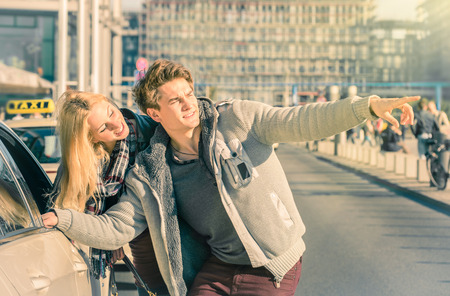 Young couple of lovers dealing with a taxi cab in the city center - Handsome man and beautiful woman explaining street directions to taxicab - Sunny day of a love story on a warm vintage filtered lookの写真素材