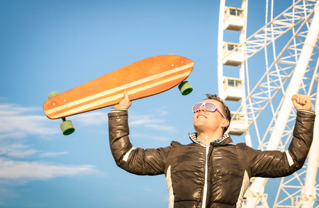 Young hipster man with longboard skate board at luna park - Concept of modern vintage alternative...