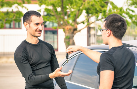 Happy satisfied young man receiving car keys after second hand sale - Concept business transport trade of modern luxury vehicles - Car rental assistance and insurance customer careの写真素材