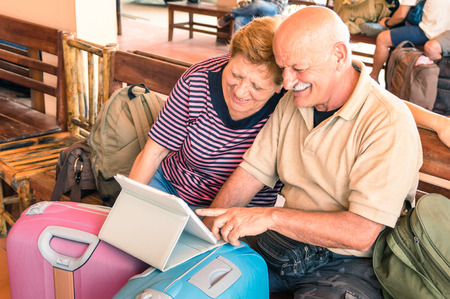 Happy senior couple sitting with digital laptop and travel baggage during adventure trip around the world - Concept of active elderly lifestyle and interaction with new trends and technologiesの写真素材