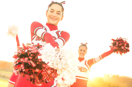 Group of cheerleaders performing outdoors  - Concept of cheerleading team sport training at high school during sunset - Tilted horizon composition and warm filter with sun backlightingの写真素材