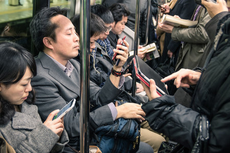 TOKYO -MARCH 2, 2015: people busy with smartphones and tablets in the underground train. The combination of the subway network of the Tokyo and Toei metros, comprises 290 stations and 13 lines. TOKYO -MARCH 2, 2015: people busy with smartphones and tablets in the underground train. The combination of the subway network of the Tokyo and Toei metros, comprises 290 stations and 13 lines.