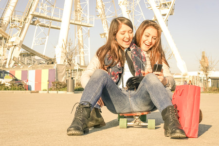 Best friends enjoying time together with smartphone music playlist in a spring sunny day - New trends and technology concept with hipster girlfriends having fun outdoors - Warm vintage filtered lookの写真素材