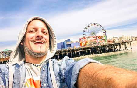 Handsome man taking a selfie at Santa Monica Pier with ferris wheel の写真素材