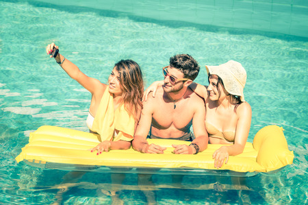 Best friends taking selfie at swimming pool with yellow airbed 