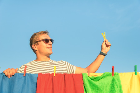 Young handsome hipster man hanging colorful laundry with clothespin - Concept of single lifestyle...