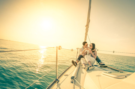 Young couple in love on sail boat with champagne at sunset - Happy exclusive alternative lifestye concept  - Soft focus due to backlight on vintage nostalgic filter - Fisheye lens and tilted horizonの素材 [FY31039317123]