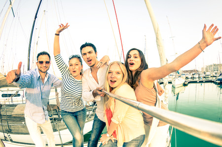 Best friends using selfie stick taking pic on exclusive luxury sailing boat - Concept of friendship and travel with young people and new technology  trends - Bright nostalgic desaturated color tonesの写真素材