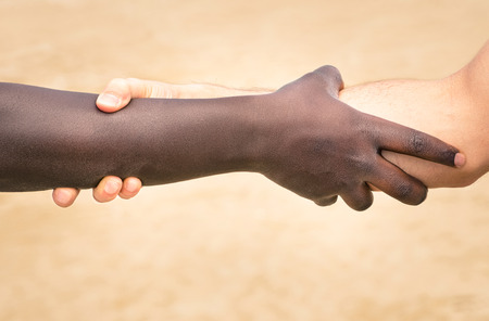Black and white hands in modern handshake to show each other friendship and respect - Helping and respecting each other against racism - Slightly crispy detailed filtered look on defocused backgroundの写真素材