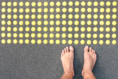 Naked human barefoot on asphalt road at tactile bumps paving - Life concept of human feeling with bare feet of blind people on the floor sidewalk warning pad - Social welfare assistance and facilitiesの写真素材