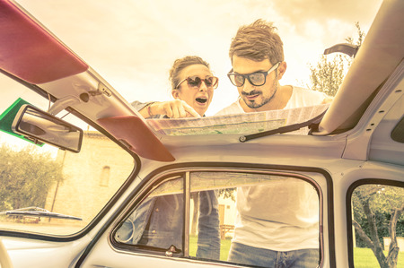 Couple of lovers looking at a map during honeymoon trip vacation - Vintage lifestyle traveling around the world with old retro classic car - Young people enjoying together happy moments of lifeの写真素材