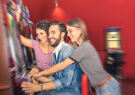 Happy young friends having fun together with slot machine - Gambling concept with people playing at cash automatic devices in modern casino and resort - Blurred edges with soft radial zoom defocusingの写真素材