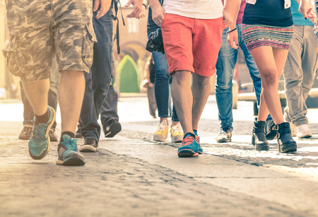 Crowd of people walking on the street - Detail of legs and shoes moving on sidewalk in city center - Travellers with multicolor clothes on vintage filter - Shallow depth of field with sunflare halo