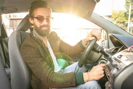 Young hipster fashion model driving car - Young confident man with beard and alternative mustache smiling looking at camera - Warm filter with soft focus on the face due to natural sun flare haloの写真素材
