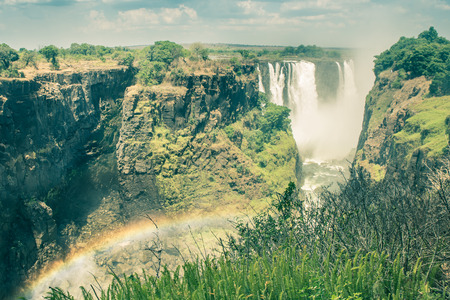 Side view of Victoria Waterfalls with rainbow natural effect - World famous nature wonder of Zimbabwe and Africa continent - Vintage filtered lookの写真素材