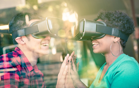 Multiracial couple in love going beyond racial diversity through virtual reality glasses - Young people having fun using new technology - Composition with window reflection on enhanced sun flare haloの写真素材