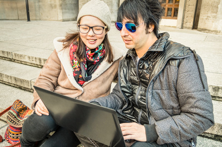 Multiracial couple having fun using laptop - Modern concept of connection with computer technology - City urban lifestyle and everyday life rapport - Main focus on girl with warm desaturated filterの写真素材