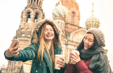 Happy girlfriends taking winter selfie at " Savior on Spilled Blood " church in Saint Petersburg - Friendship concept with girls having fun together drinking coffee outdoor - Focus on left young womanの写真素材
