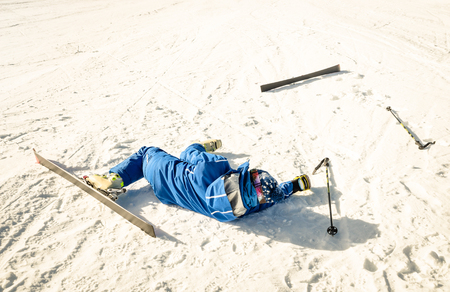 Professional skier after crash accident on skiing resort slope - Winter sport emergency concept with athlete needing help assistance on dramatic trouble situation - Warm sunny afternoon color tonesの写真素材