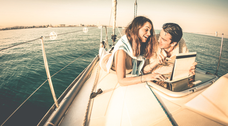 Young couple in love on sail boat having fun with tablet - Happy luxury lifestyle on yacht sailboat - Technology interaction with satellite wifi connection - Retro contrasted filterの写真素材