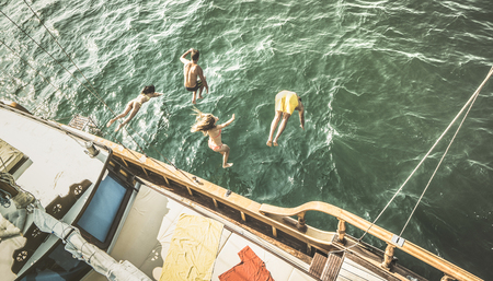 Aerial view of young people jumping from sailing boat on sea trip - Rich happy friends having fun in summer sailboat party day - Exclusive luxury vacation concept - Retro contrast desaturated filterの写真素材