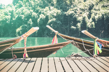 Longtail boats at Cheow Lan Lake on wooden jetty pier docks - Khao Sok national park in Thailand - Adventure travel concept with wanderlust feelings - Azure turquoise filter on sunflare halo sunshineの写真素材