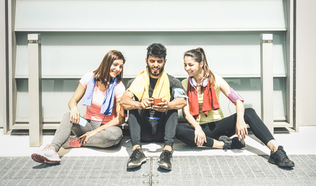 Happy friends having a break during sport fitness training using mobile smart phone - Young sporty...