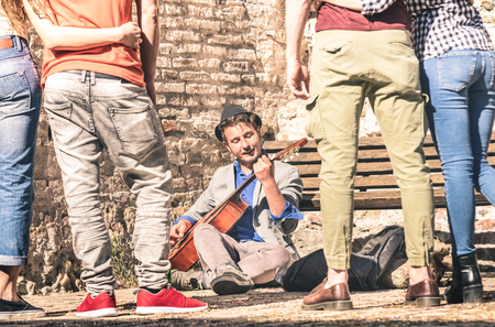 Young people watching street artist performer playing acoustic classic guitar outdoors - Adventure lifestyle concept with musician guy earning money with artistic skills - Warm afternoon filter tonesの写真素材