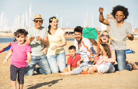 Happy multiracial families and children playing together with kite at beach vacation - Multicultural summer joy concept with mixed race people having candid genuine fun  - Warm afternoon color tonesの写真素材