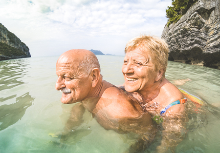 Senior couple vacationer having genuine playful fun on tropical beach in Thailand - Snorkel tour in exotic scenario - Active elderly and travel concept around the world - Warm afternoon bright filterの写真素材