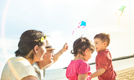 Happy family with parents and children playing together with kite at beach vacation - Summer joy concept with mixed race people having pure genuine fun together  - Warm sunshine backlight filterの写真素材