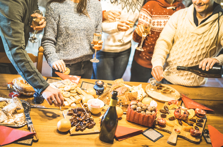 Side view of friends group tasting christmas sweets food and having fun at home drinking champagne sparkling wine - Winter holidays concept with people enjoying time eating together - Warm filterの写真素材