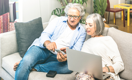 Senior retired couple using laptop computer at home on sofa - Elderly and technology concept with mature people at online shopping - Modern situation of internet connection booking - Neutral filterの写真素材