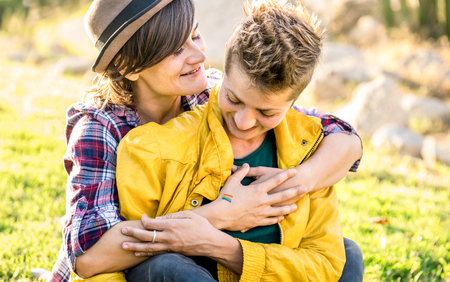 Young girlfriends in love sharing time together at travel trip hugging at park - Playful women friendship concept with girls couple having fun on fashion clothes outdoors - Bright warm sunshine filterの写真素材