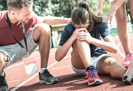 Female athlete getting injured during athletic run training - Male coach taking care on sport pupil after physical accident - Team care concept with young sporty people facing mishaps casualtyの写真素材