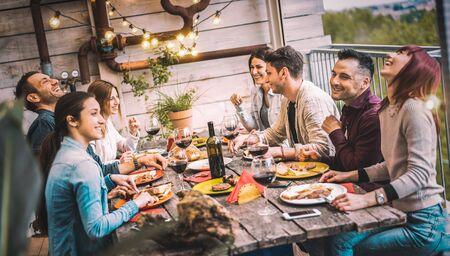 Young people dining and having fun drinking red wine together on balcony rooftop dinner party - Happy friends eating bbq food at restaurant patio - Millannial life style concept on warm evening filterの写真素材