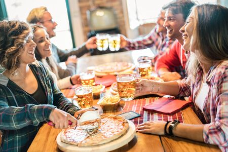 Young friends eating pizza at home on winter reunion - Friendship concept with happy people enjoying time together and having fun drinking brew pints - Cosy dinner place with focus on beer glassの写真素材