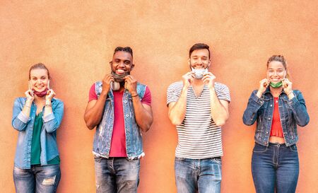 Multiracial millennial friends smiling with face mask after lockdown reopening - Happy guys and girls having fun around old town streets - University students on travel vacation  - Warm bright filterの写真素材
