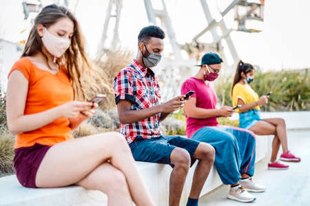 Multicultural friends with surgical mask using tracking app on mobile smart phones - Bored young...