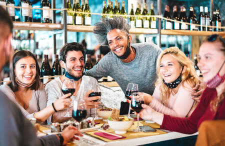 Friends drinking red wine at sushi bar restaurant with open face masks - New normal lifestyle...